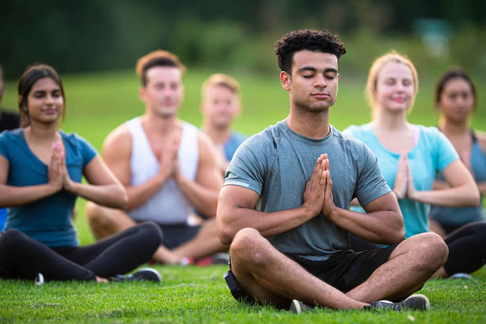 A group of middle-aged people doing yoga and meditation in a grassy field